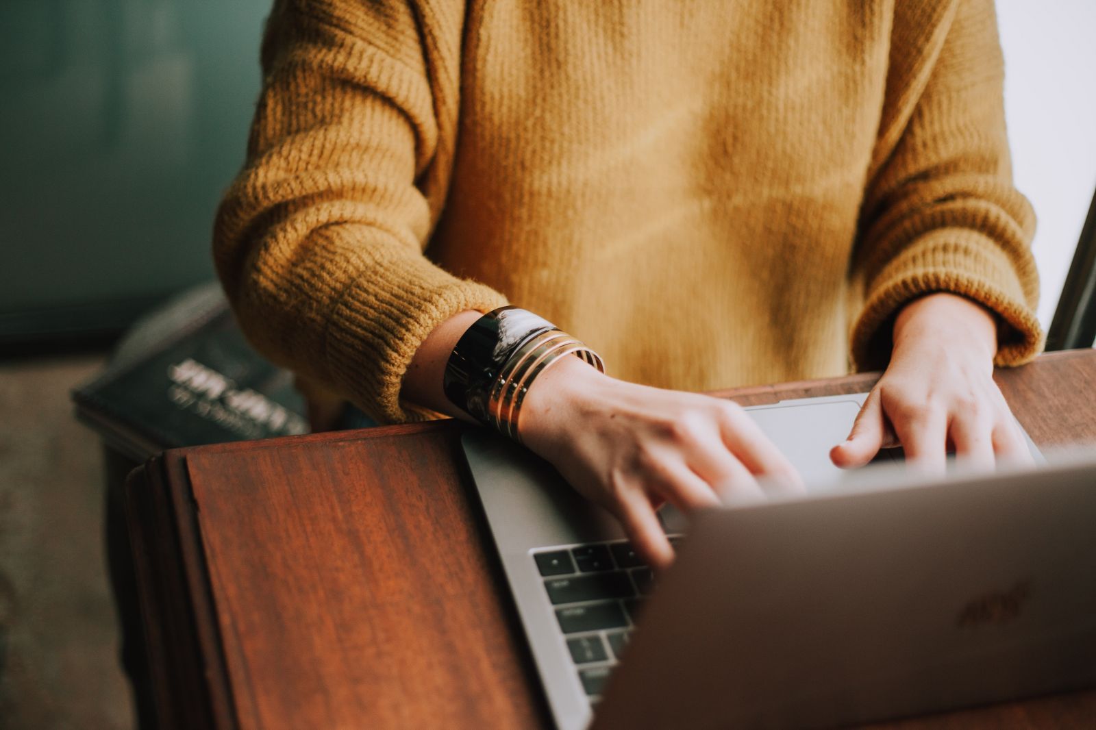 young woman in mustard sweatshirt typing on a laptop