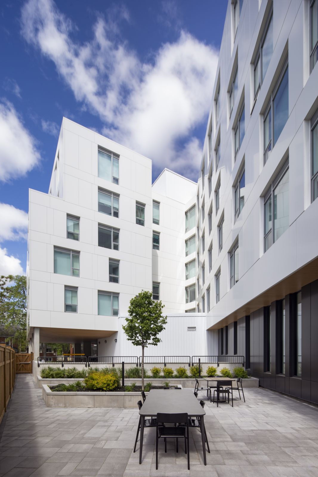 GEOpark courtyard with white apartment walls, paved seating area, tables, and young trees.